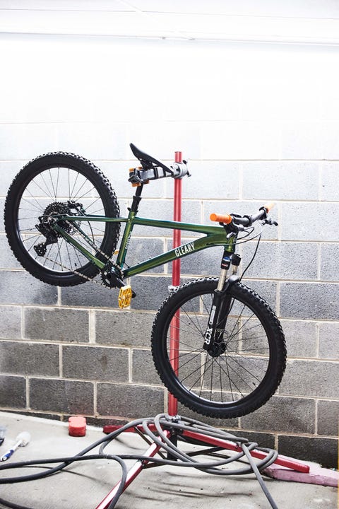 green cleary bike hanging off of a stand against a white spray painted brick wall