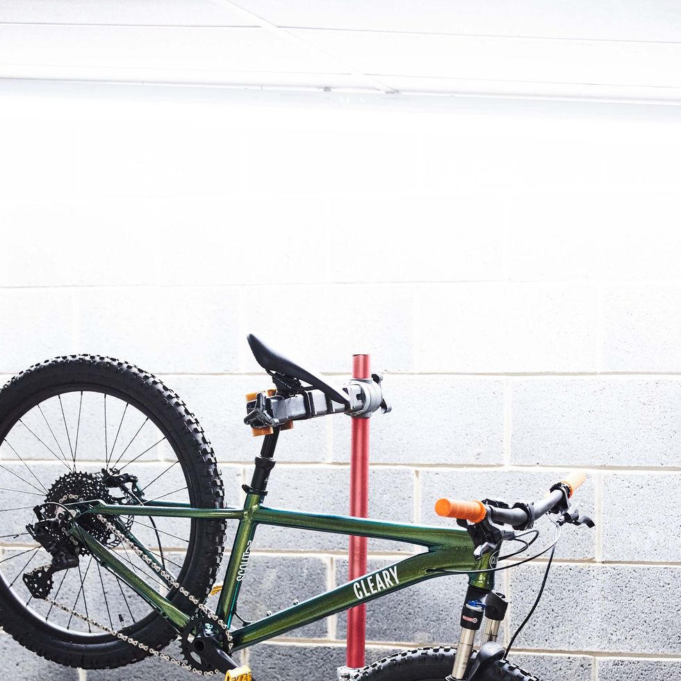 green cleary bike hanging off of a stand against a white spray painted brick wall