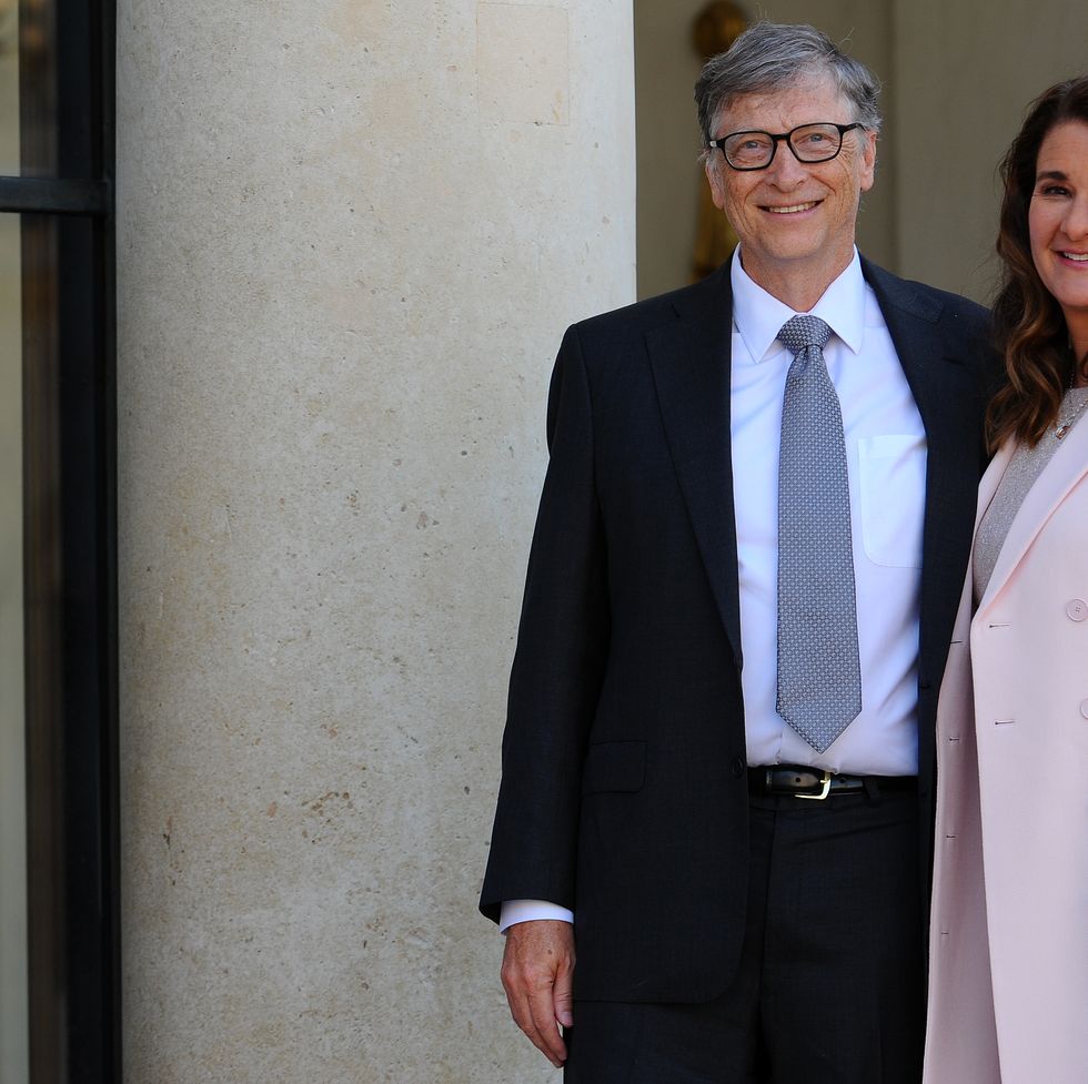 bill gates and melinda gates smile at the camera while standing in front of a concrete pillar