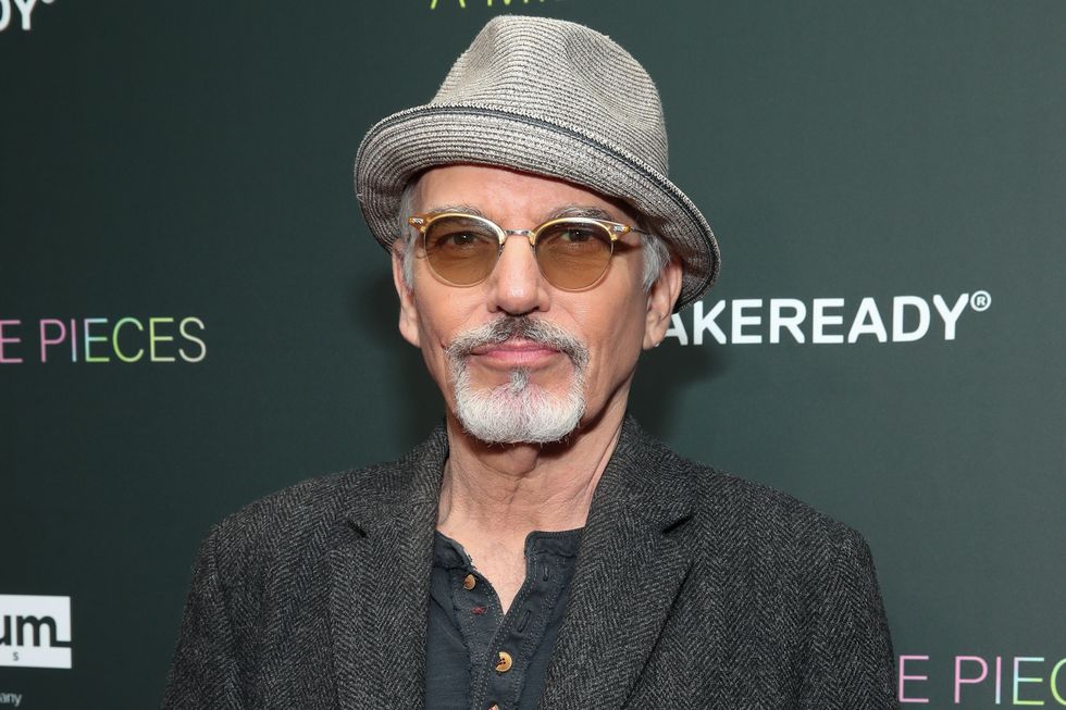 billy bob thornton wearing a dark grey top and jacket, light grey hat and shaded glasses, a neutral expression on his face looking at the camera, an older man with greying hair and beard