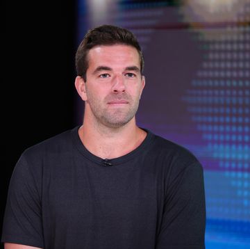 billy mcfarland wearing a t shirt and looking out of frame in front of a blue background