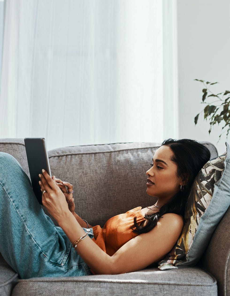 woman sitting on couch holding a tablet and watching a show, giving up your favorite streaming service for lent