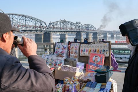 Een man bekijkt de koopwaar van een souvenirstalletje in Dandong vlakbij de ChineesNoordKoreaanse Vriendschapsbrug De brug werd in de Koreaanse Oorlog door de VS gebombardeerd en later herbouwd maar een gedeelte van de Gebroken Brug is nu een oorlogsmonument