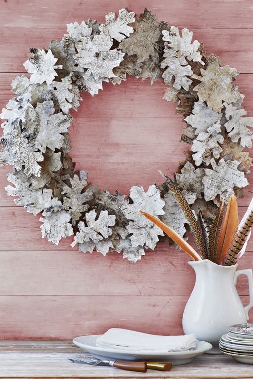 fall wreath crafted from leaf shapes cut from birch bark, hung on red washed rustic wood wall above pitcher of feathers