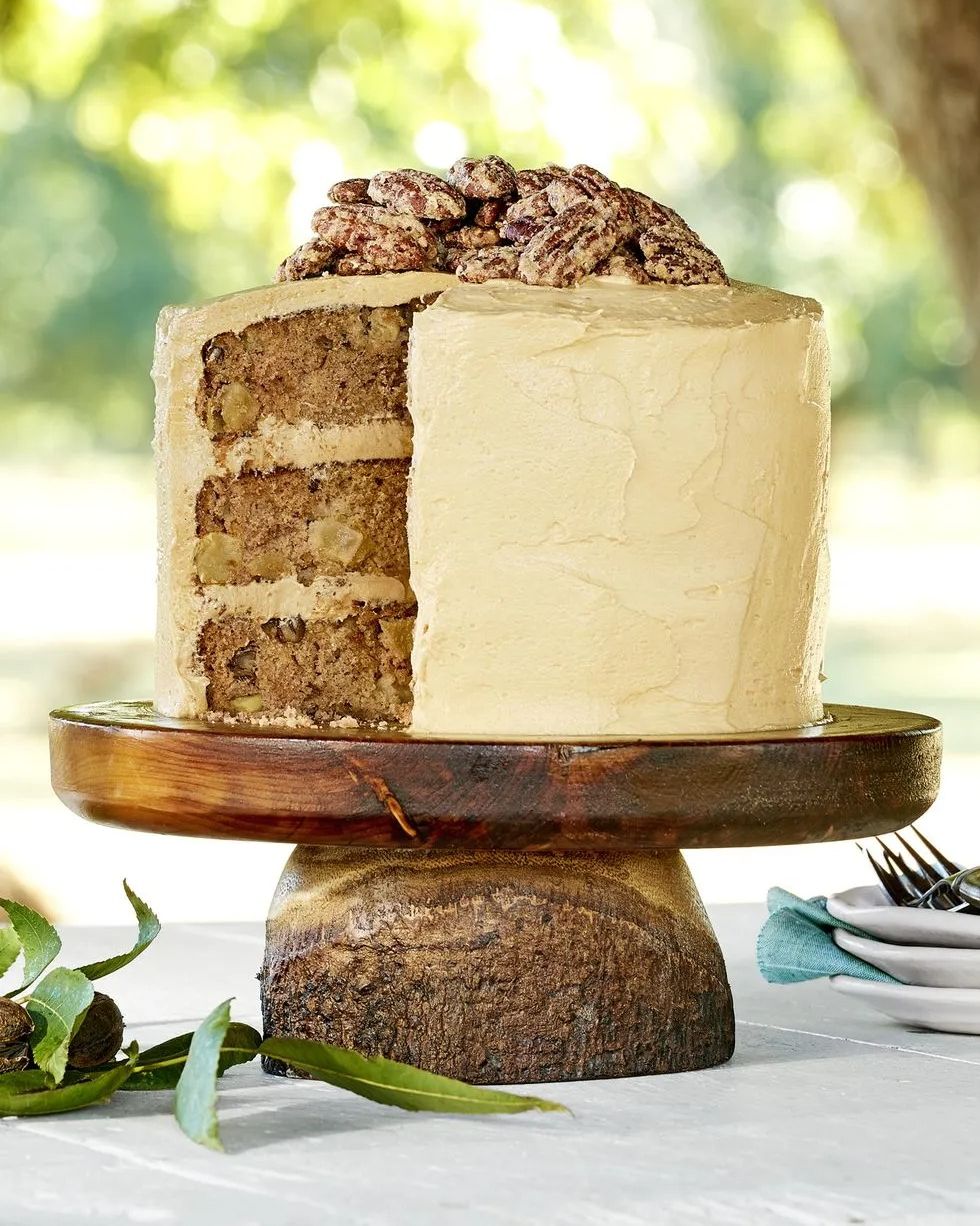 three layer apple cinnamon cake on a wooden cake stand with sugared pecans on top