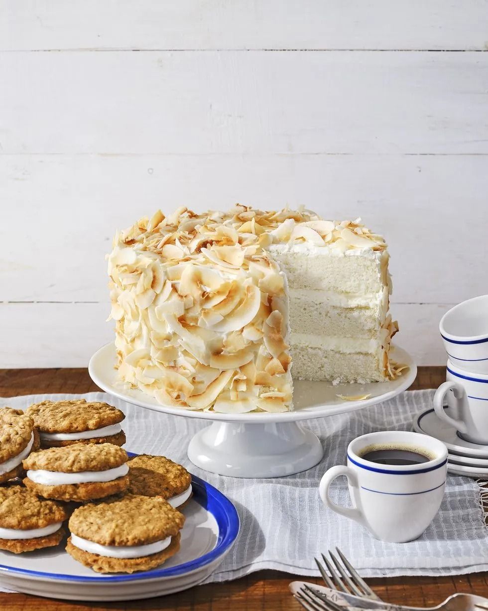 three layer coconut angel cake covered with toasted coconut on a white cake stand