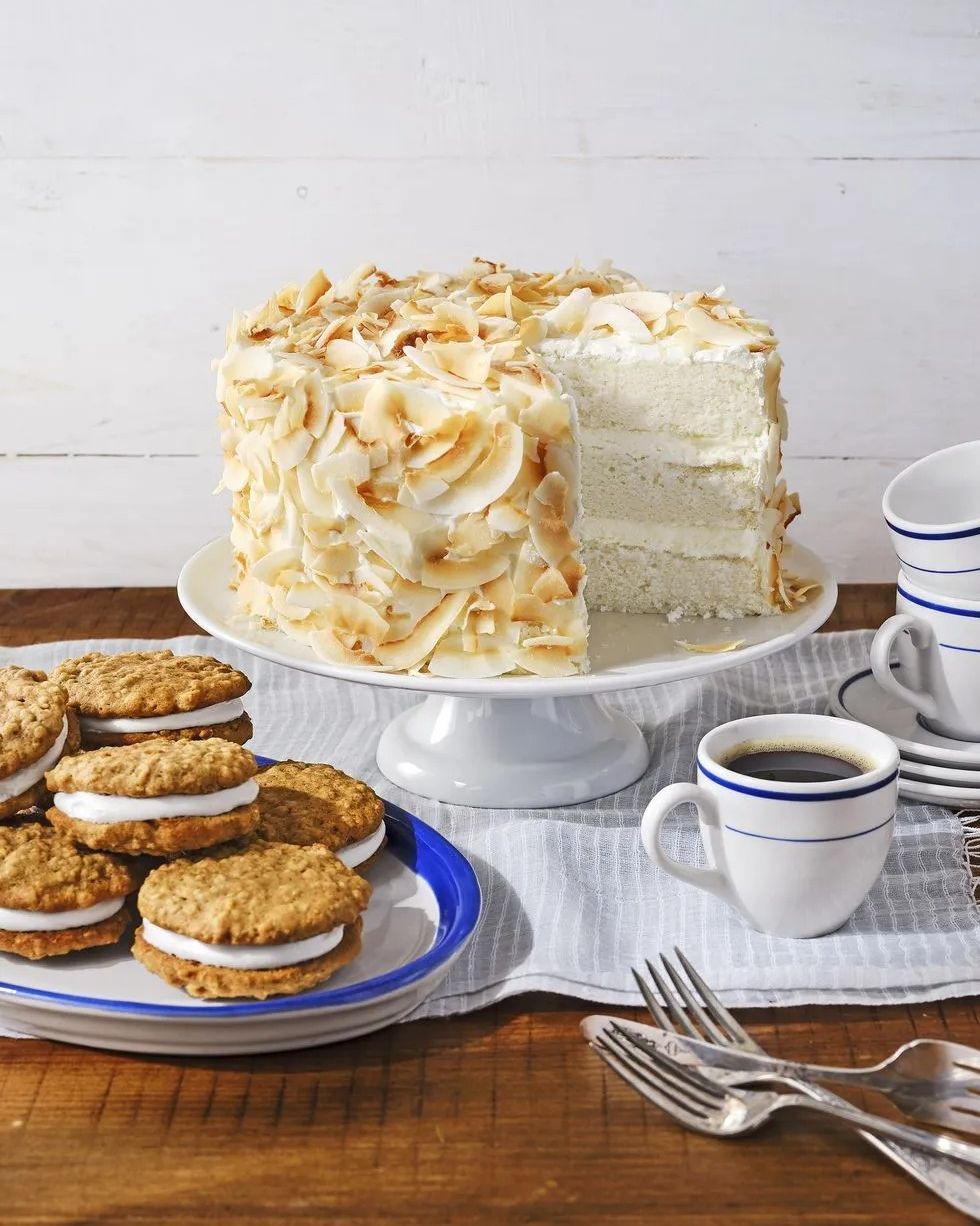 three layer coconut angel cake covered with toasted coconut on a white cake stand