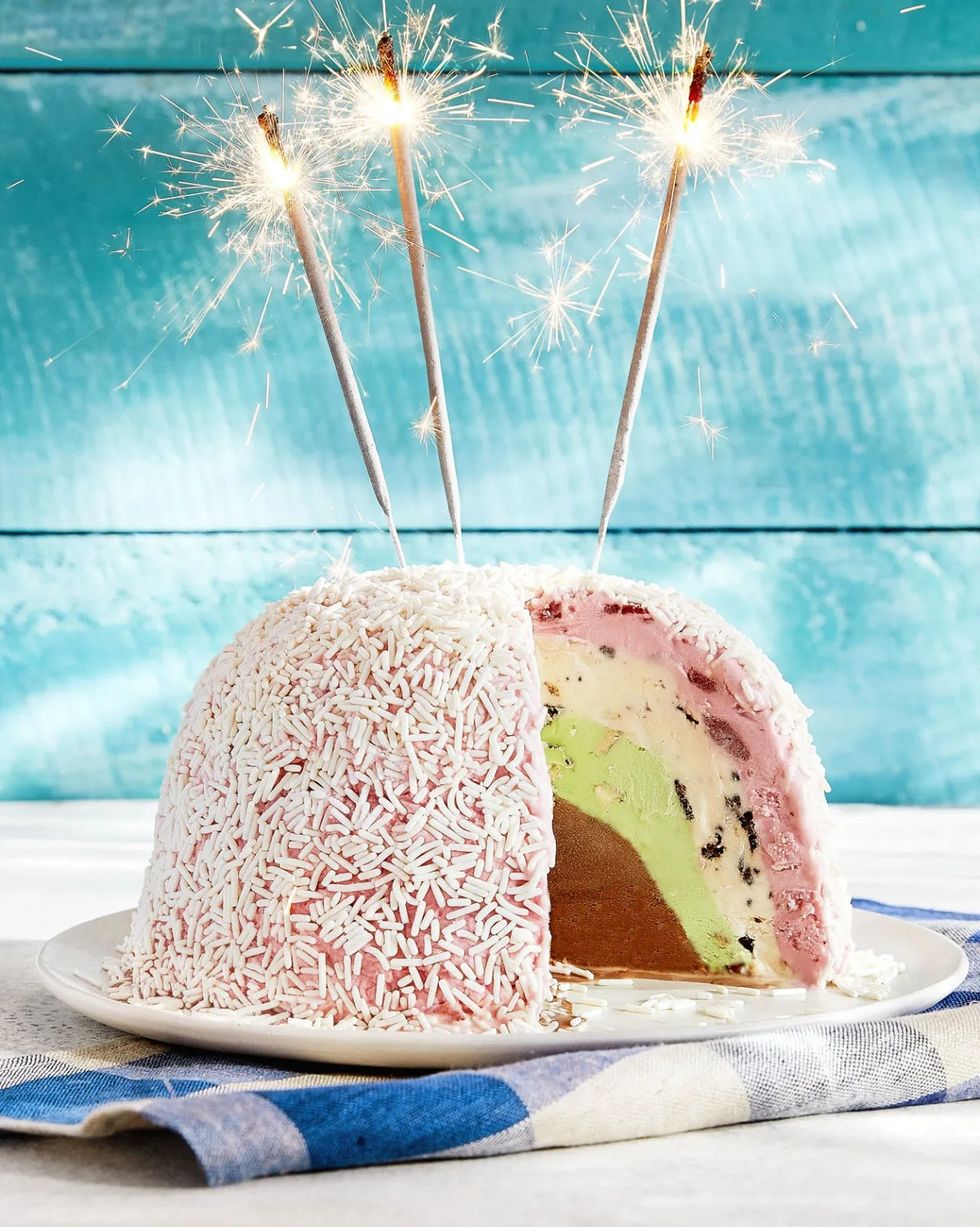 ice cream bombe covered in white sprinkles with three sparkler candles on top