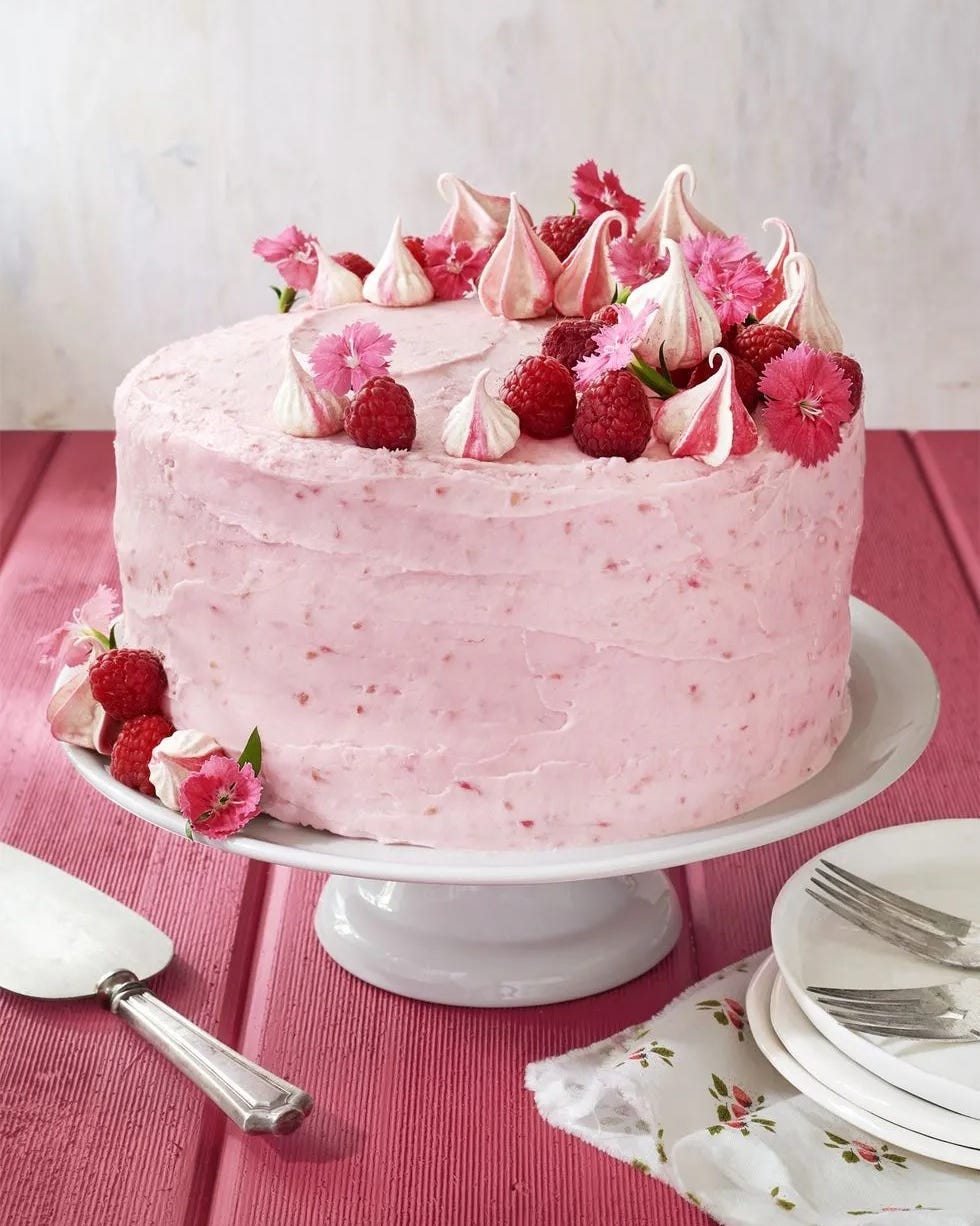 raspberry pink velvet cake with raspberries meringue cookies and flowers around the top