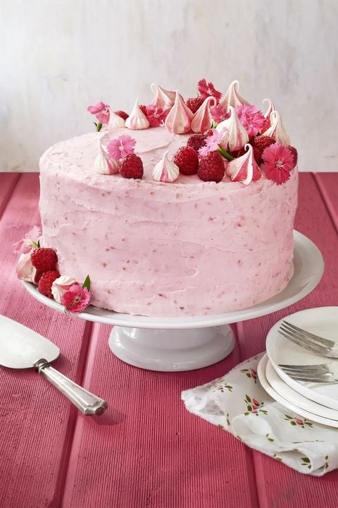raspberry pink velvet cake with raspberries meringue cookies and flowers around the top