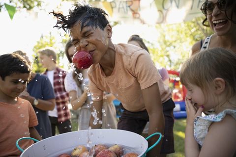 Playful boy splashing, bobbing for apples at summer neighborhood block party in park
