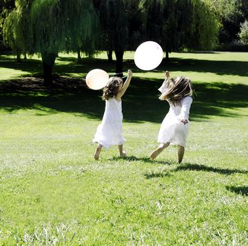 two girls running through field with balloons