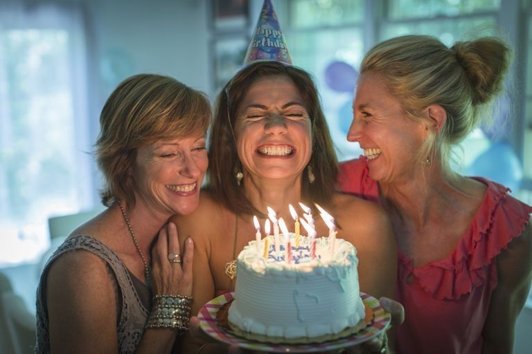 women singing happy birthday with cake