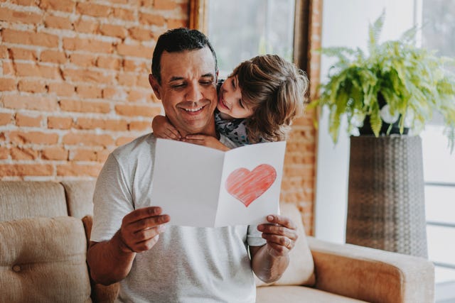 little boy hugging dad as he reads a card on the couch