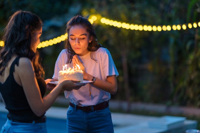 two female friends celebrating at a birthday party as one blows out the candles on a birthday cake