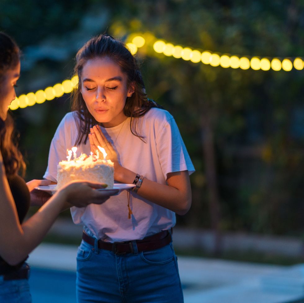two female friends celebrating at a birthday party as one blows out the candles on a birthday cake