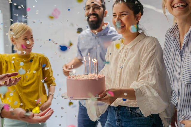 a woman carries a birthday cake celebrating with a group of people and confetti in the air