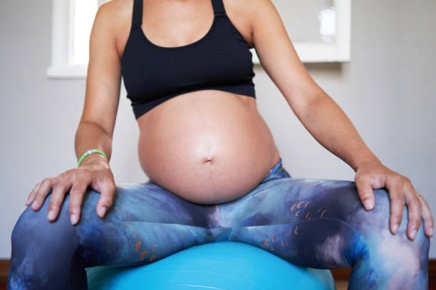 front view of pregnant woman sitting on gymball doing pilates exercises for pregnant women