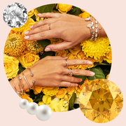 two womens hands with birthstone gem bracelets and rings displayed against yellow flowers