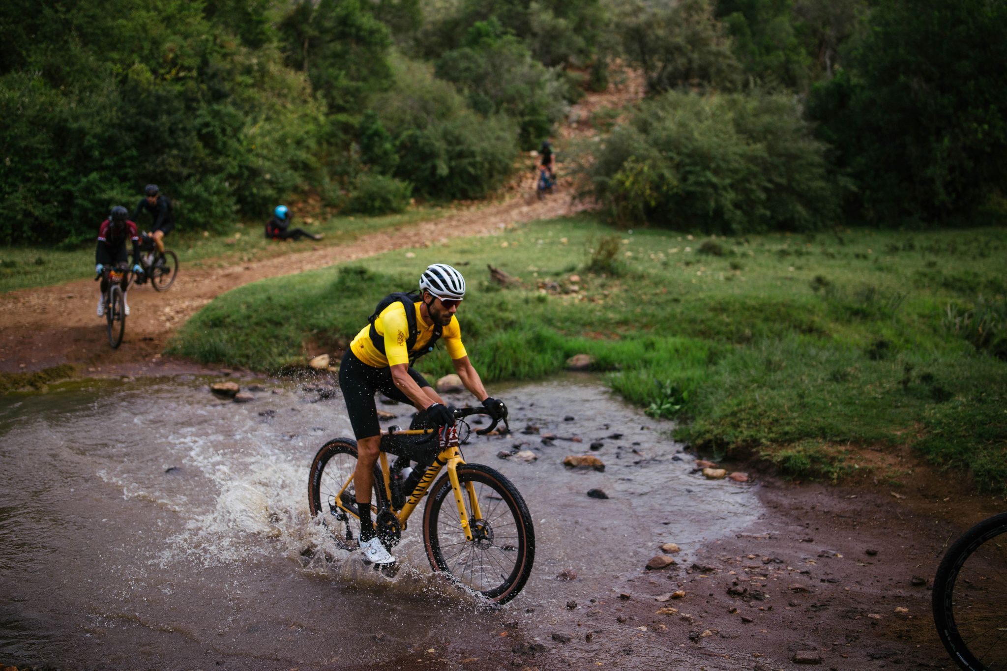 a cyclist rides across a creek on a dirt road