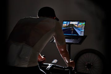 Cyclist using a stationary bike with a laptop displaying a virtual cycling environment