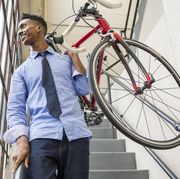 Black businessman descending staircase carrying bicycle
