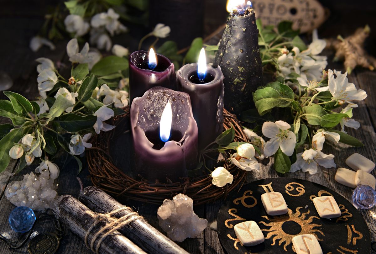 Black candles with runes, zodiac circle and spring flowers