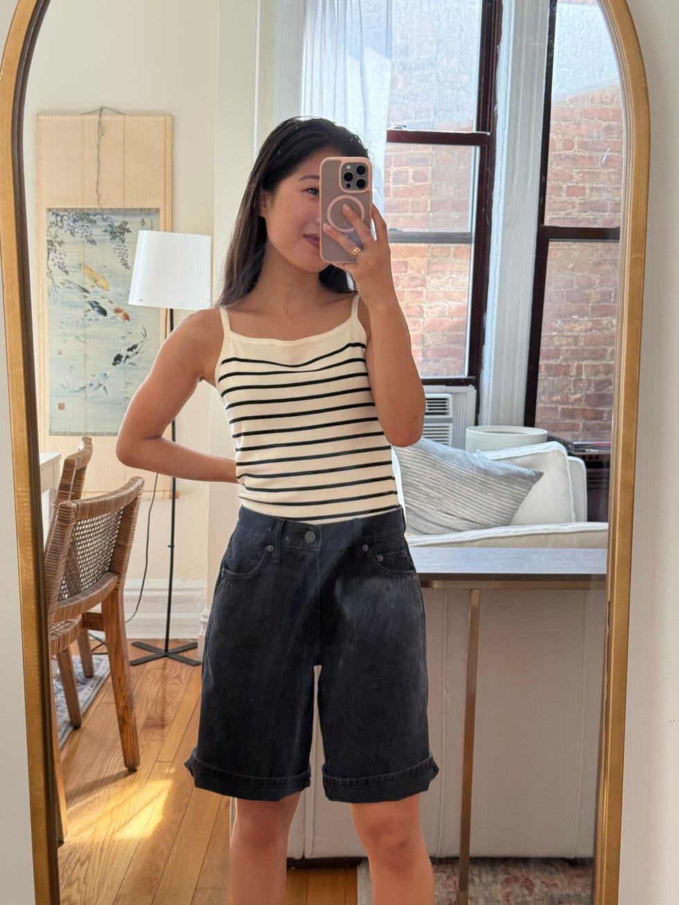 person in a striped tank top and denim shorts standing in front of a mirror