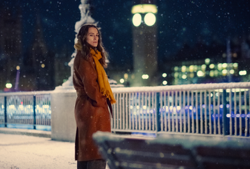 person standing on a snowy sidewalk at night near a clock tower