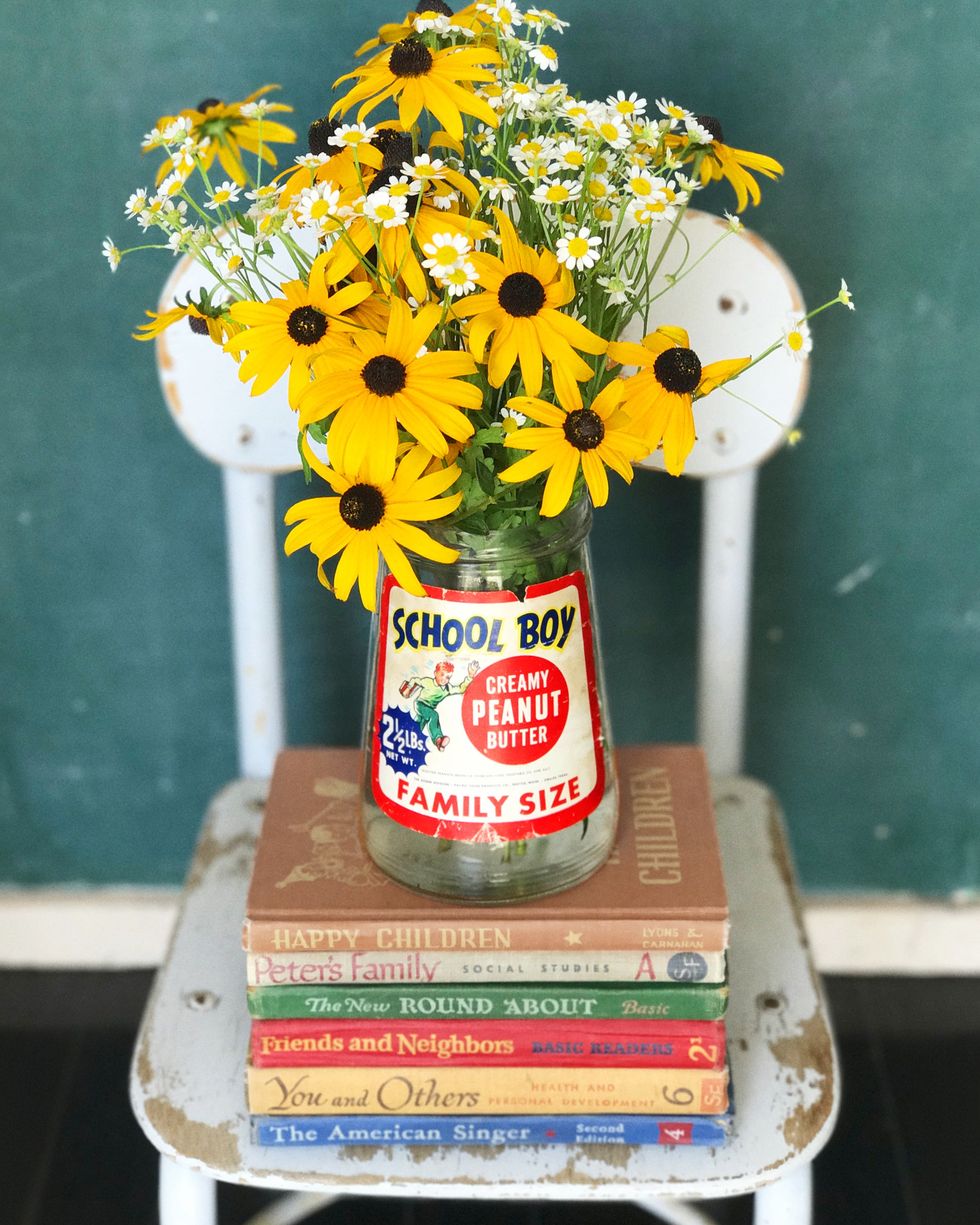 bouquet of black eyed susans in glass peanut butter jar on top of stacked children’s books