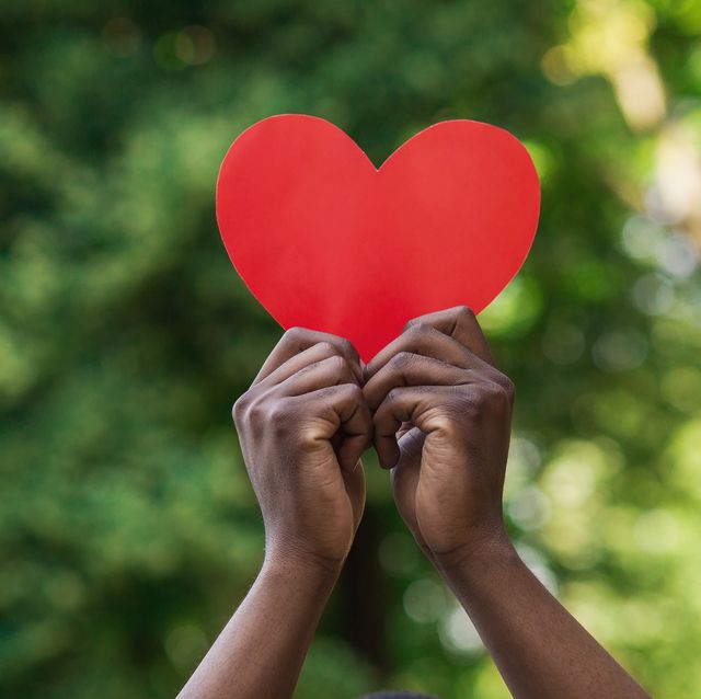 black hands holding red paper heart on green background