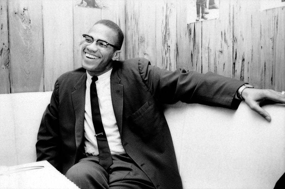 black and white photo of malcolm x sitting in a booth, smiling