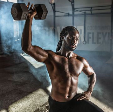 Black male athlete exercising with dumbbell in lunge position at gym.