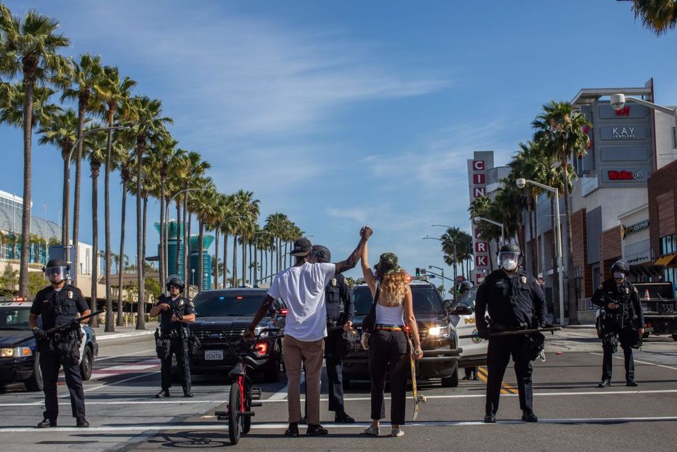 a black man and a white woman hold their hands up in a front of police officers in downtown long beach on may 31, 2020 during a protest against the death of george floyd