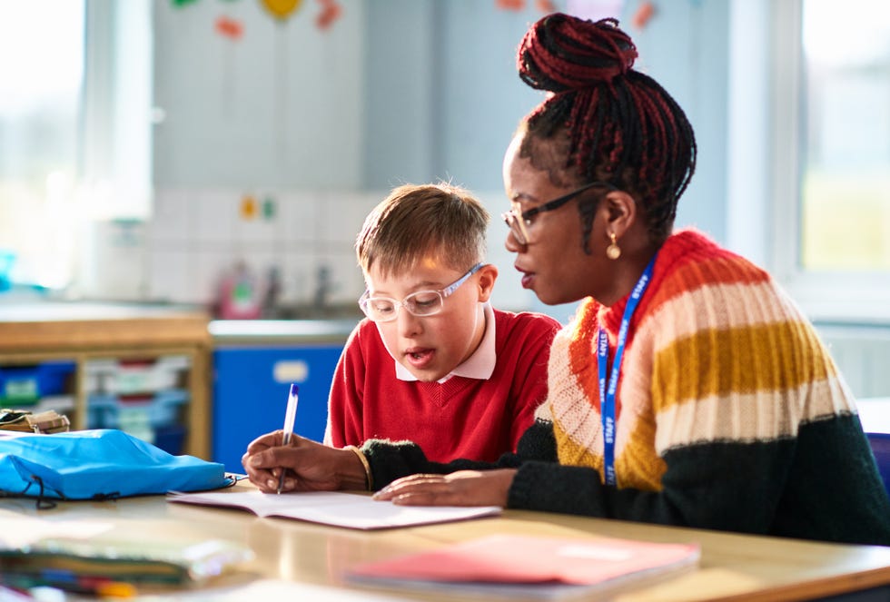 black mid adult primary school teacher helping boy with down syndrome in classroom