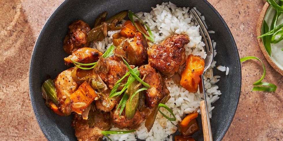 black pepper chicken with orange peppers, celery and scallions over white rice in a black bowl
