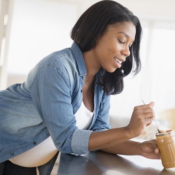 black pregnant woman eating peanut butter in kitchen