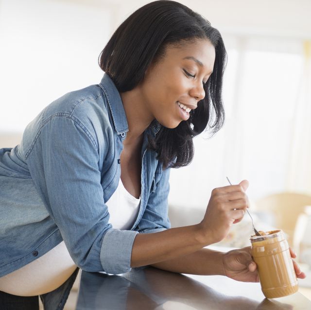black pregnant woman eating peanut butter in kitchen
