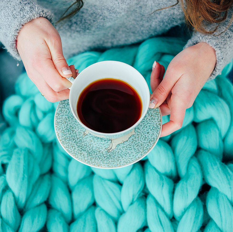 feminine hands holding cup of black tea over teal cozy knitted blanket