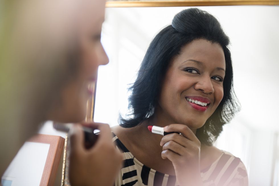 a woman applies red lipstick in a mirror