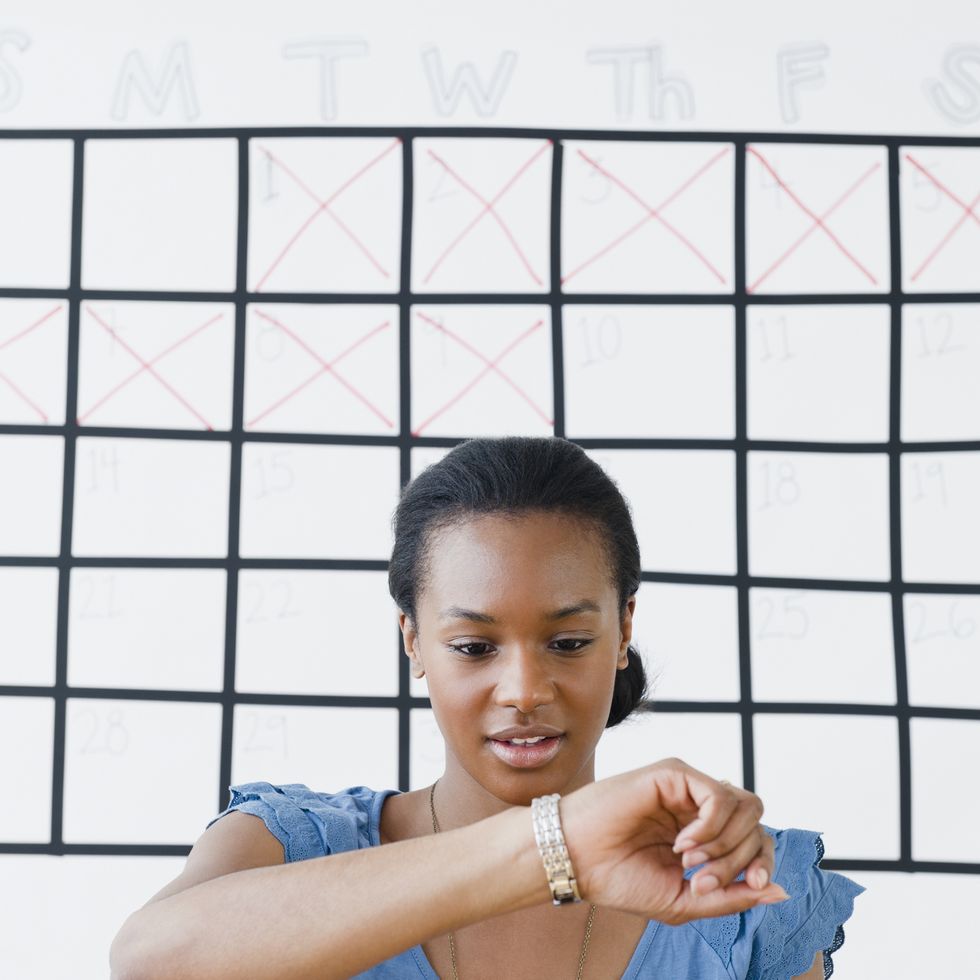 black woman checking her wristwatch in front of a calendar
