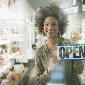 black woman holding open sign in store window