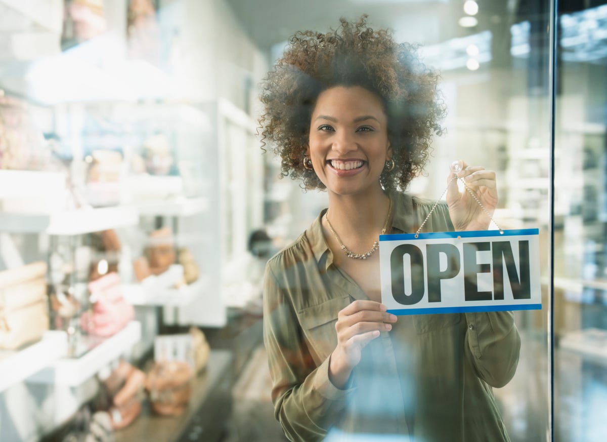 black woman holding open sign in store window