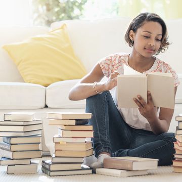 black woman sitting on floor reading pile of books