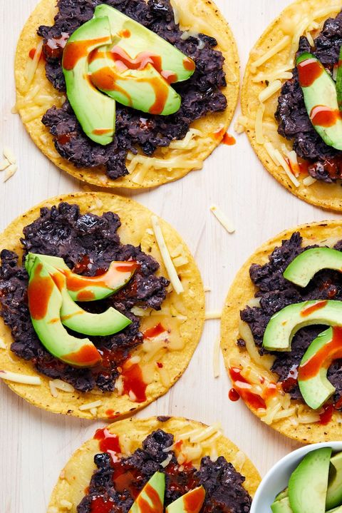 black bean tostadas topped with avocado and hot sauce on a white wooden background