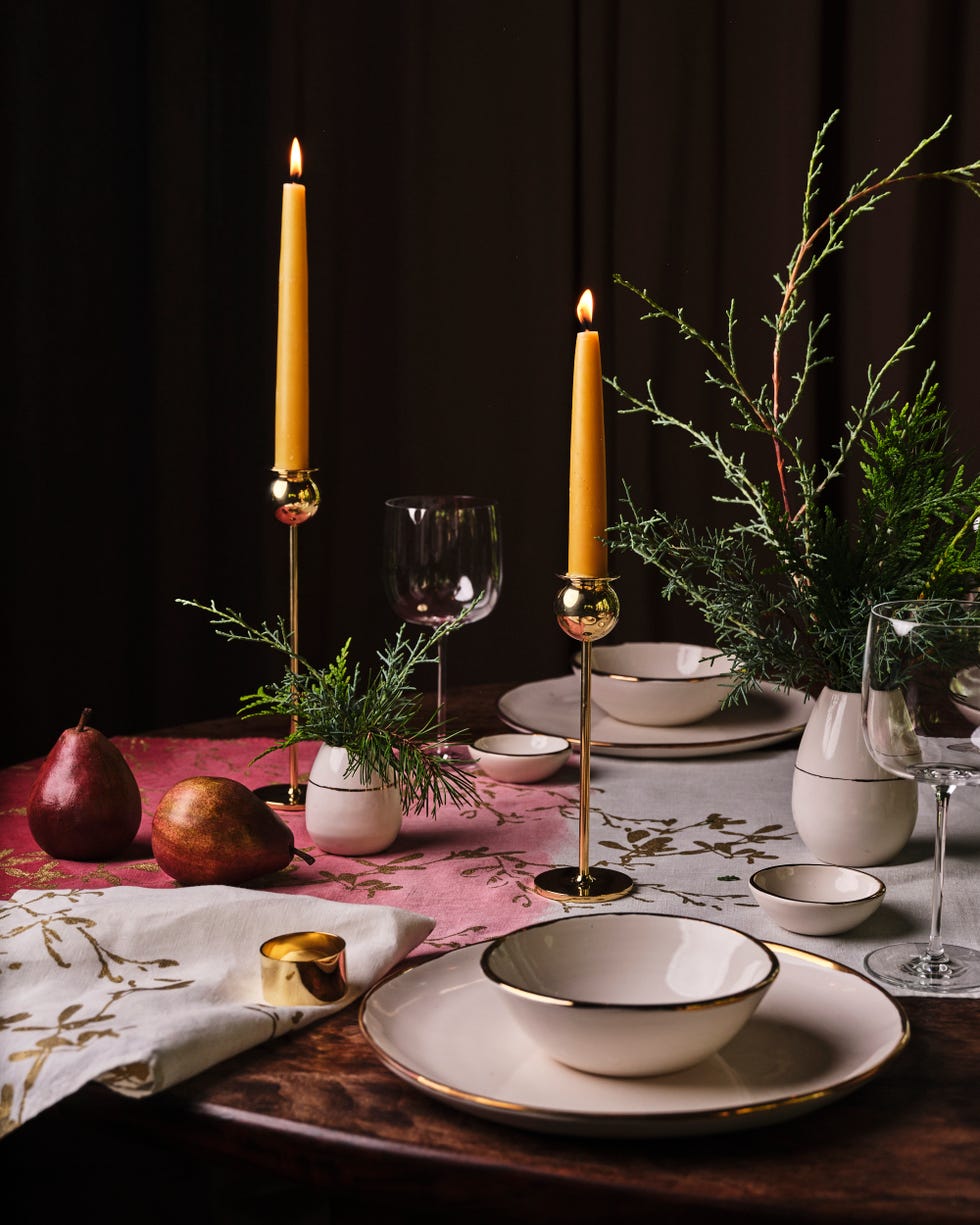 gold candlesticks on a table with cedar sprig centerpieces and white porcelain table settings