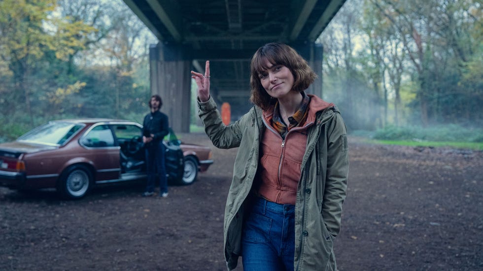 person gesturing near a car under an overpass in a wooded area