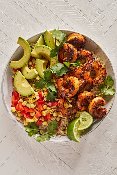 bowl of brown rice topped with blackened shrimp, grilled corn, chopped red peppers, lime wedges, and cilantro
