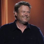 blake shelton stands smiling on stage with microphone in hand