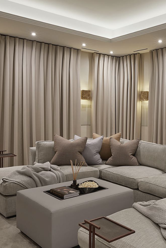 home theater with drapes on the walls, large grey couch with pillows and blankets